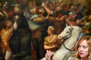 Giorgia Meloni stands in front of a painting depicting people and horses