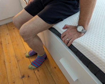 The reviewer’s husband sits at the edge of the Emma Hybrid Premium Mattress.