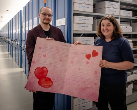 Dominik Taubert and Carla Cron hold open a large pink card with hearts on it