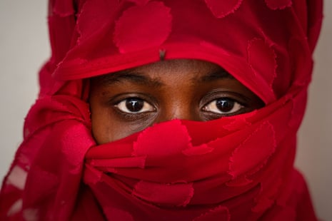 A woman looks directly at the camera. Only her eyes are visible; her face and head are wrapped in a bright red scarf.