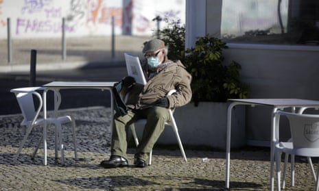 A man wearing a face mask reads a magazine in the sun outside a cafe in Lisbon. Portugal’s government has ordered a lockdown, starting Friday, after a steady resurgence of virus infections during the past few weeks.