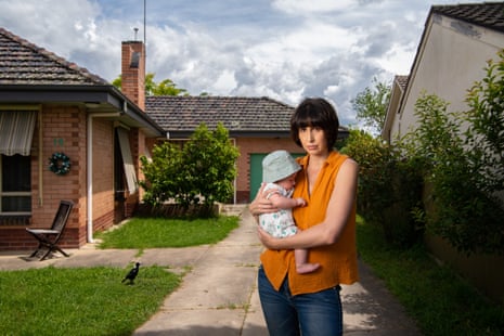 Young woman holding baby while standing in the driveway of a suburban house
