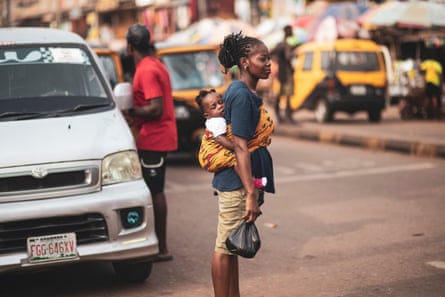 A mother with a baby tied to her back waits to cross a road A mother with a baby tied to her back waits to cross a road