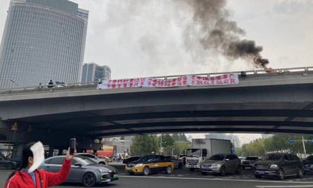 Smoke rises as a banner with a protest message hangs off Sitong Bridge in Beijing on 13 October.