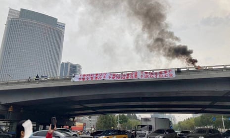 Smoke rises as a banner with a protest message hangs off Sitong Bridge in Beijing in October 2022
