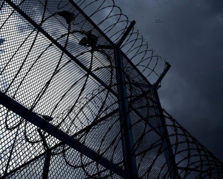 The top of a barbed wire prison fence against the sky.