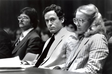 a man sits between others at the defence table, looking sideways with a serious expression