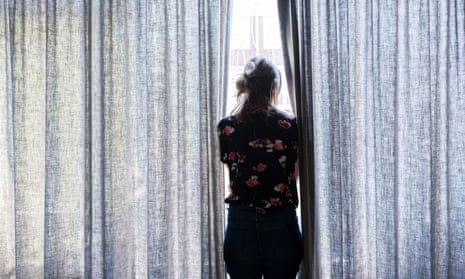 A woman looks outside a curtained window