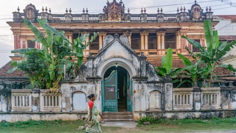 An Indian woman in a sari walks past an ornate mansion