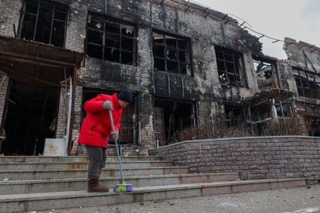 A woman cleans the stairs near a shop after shelling in the village of Liptsi in Kharkiv.