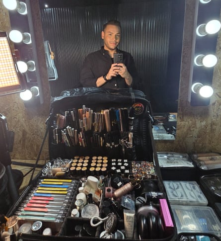A man of colour with a huge range of makeup in front of him.