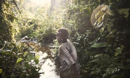 A smiling boy looks over his shoulder at the camera as he runs through dense rainforest