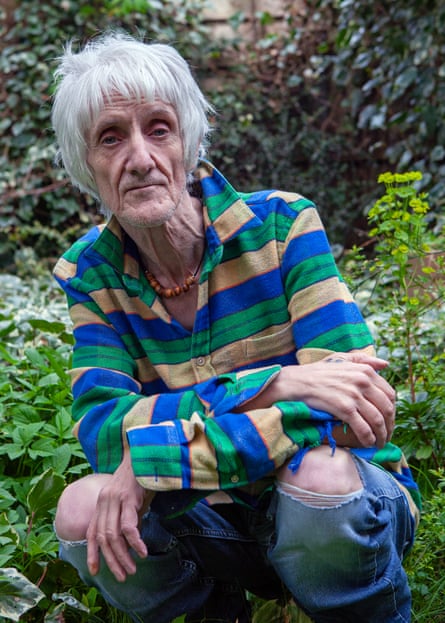 Reilly in 2021 squatting in a garden wearing a boldly striped shirt and torn jeans