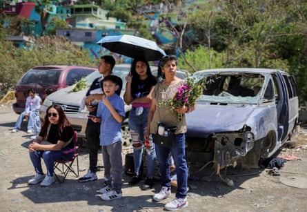People watch a lucifer adjacent to a battered car