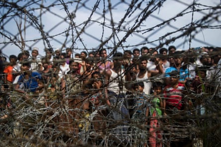 Rohingya refugees gather behind a barbed wire fence in a border zone between Myanmar and Bangladesh