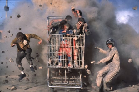 Dust and rubble fly explosively around a giant shopping trolley with five men in it