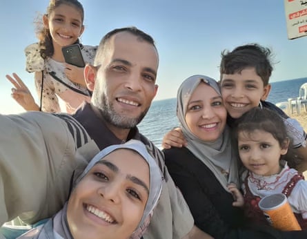 An Arab man by the sea takes a selfie, with his wife and oldest daughter in hijabs, and three younger children