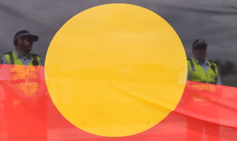 Police officers behind an Aboriginal flag 