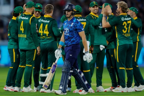 Jacob Bethell of England walks off the pitch after losing his wicket as the South Africa players celebrate.
