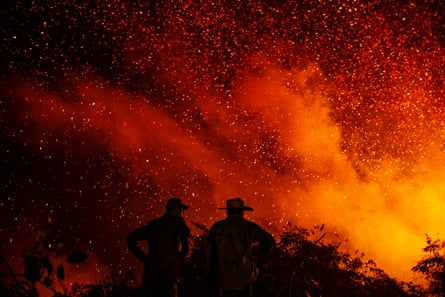 Silhouette of two firefighters standing next to a wildfire