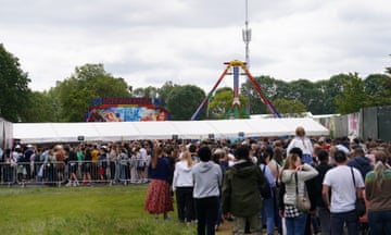 Crowds of people queue up to enter Lambeth country show. Funfair rides can be seen in the distance among trees