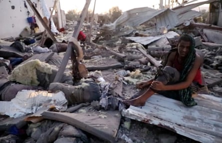 A man stares blankly as he sits amid twisted sheets of metal, rubble and possessions, while bodies can be seen nearby