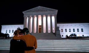 Two women embrace in front of the supreme court buidling, paying their respects to Justice Ruth Bader Ginsburg.