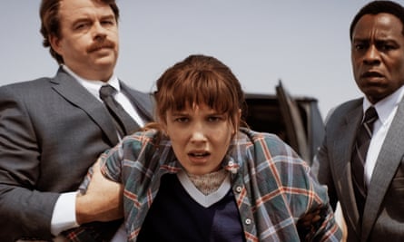 young woman in a flannel shirt being held by two men in suits