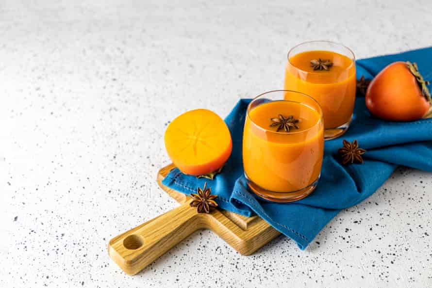 Two glasses of fresh healthy persimmon smoothie with anise stars on cutting wooden board, gray concrete background, selective focus, copy space.