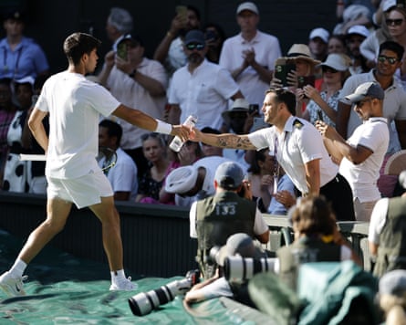 Alcaraz hands a water bottle to a security officer in the Wimbledon crowd