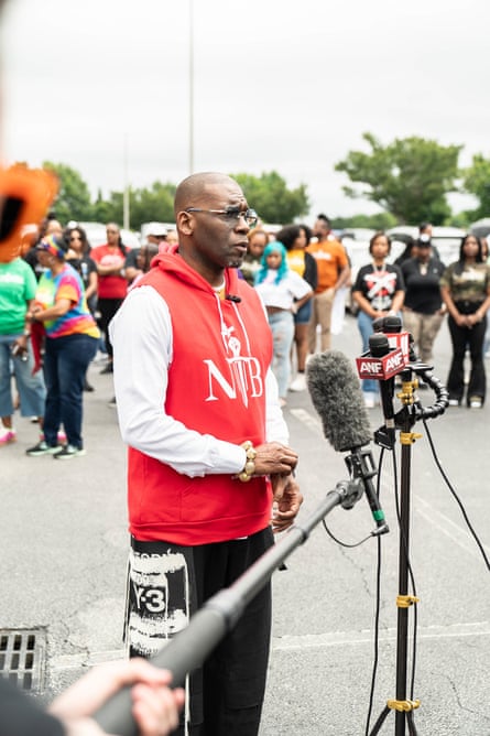 A man wearing glasses and a red sweatshirt speaks outside in a parking lot