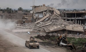 A military vehicle passes destroyed buildings in Baghouz, Syria