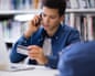A student on the phone examines a credit card while sitting near a laptop