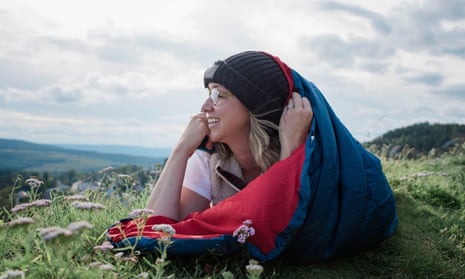Woman laying in sleeping bag on a mountain looking at the view smiling.