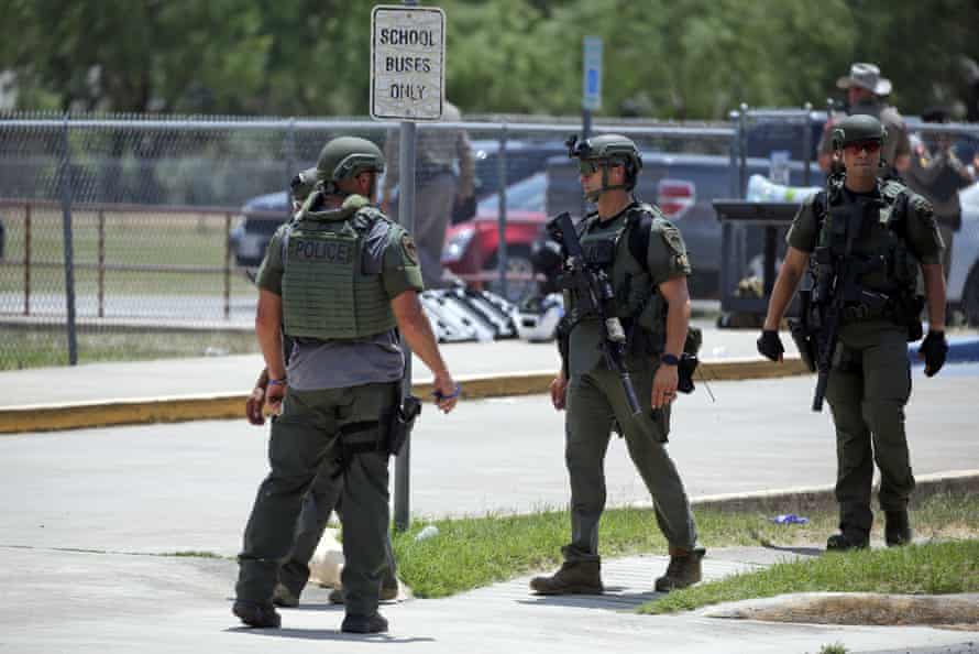 Officers wearing khaki green helmets and vests stand in a group near a sign reading 'School buses only'.