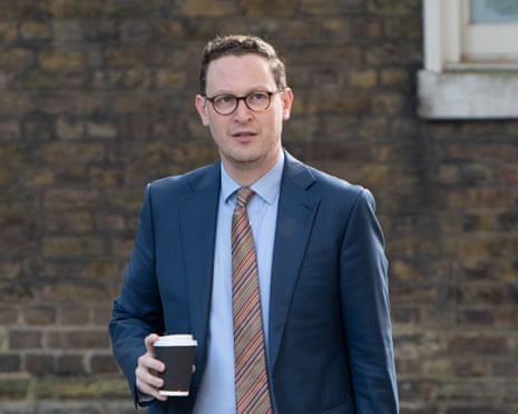 Darren Jones in glasses and a blue suit holds a coffee cup outdoors
