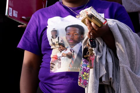 A person's torso wearing a bright purple shirt with a decal or pictures of a young Black man.