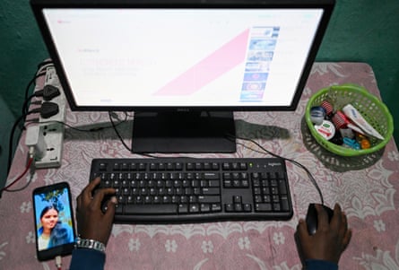 Overhead view of a hand on a keyboard and a hand on a computer mouse in front of a monitor with a phone to the side