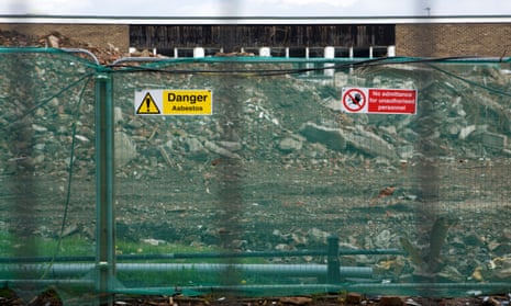 A sign warning of asbestos on a fenced-off school demolition site in the UK.