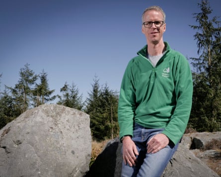 Tom Dearnley sitting on large rock with forest behind him