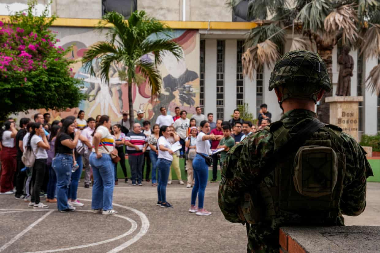 A soldier stands guard at a polling station as women queue to vote