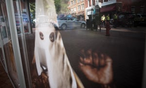 A police car is reflected in the window of a movie theatre displaying a poster for the movie BlacKkKlansman.