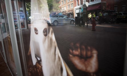 A police car is reflected in the window of a movie theatre displaying a poster for the movie BlacKkKlansman.