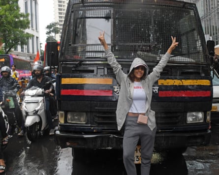 A woman in a hoodie and joggers stands in front of a police lorry or van in Mumbai, blocking it.