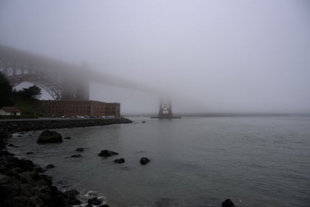 Golden Gate Bridge is barely seen in outline through dense fog over the bay; the water is grey and it is raining