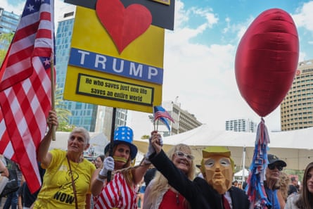 Red balloon and figure wearing Trump mask beside placard and US flag