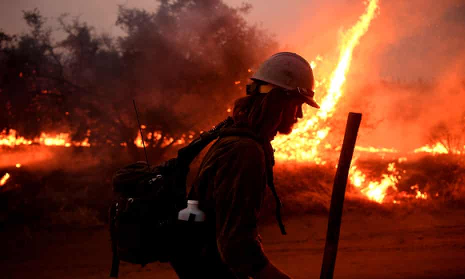 A firefighter in full gear with a helmet and backpack is semi-silhouetted against flames from the El Dorado fire.