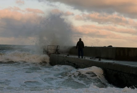 Man silhouetted by the sunset as waves crash by the pier in front of him