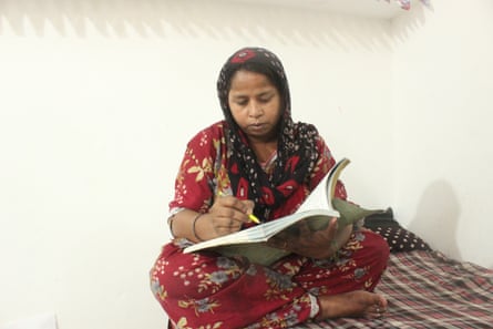 A woman in a headscarf and long robe sitting indoors writes in a book