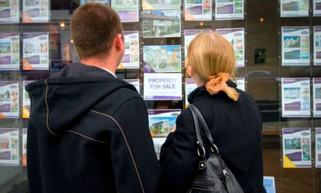 Young couple looking at houses in estate agent's window.